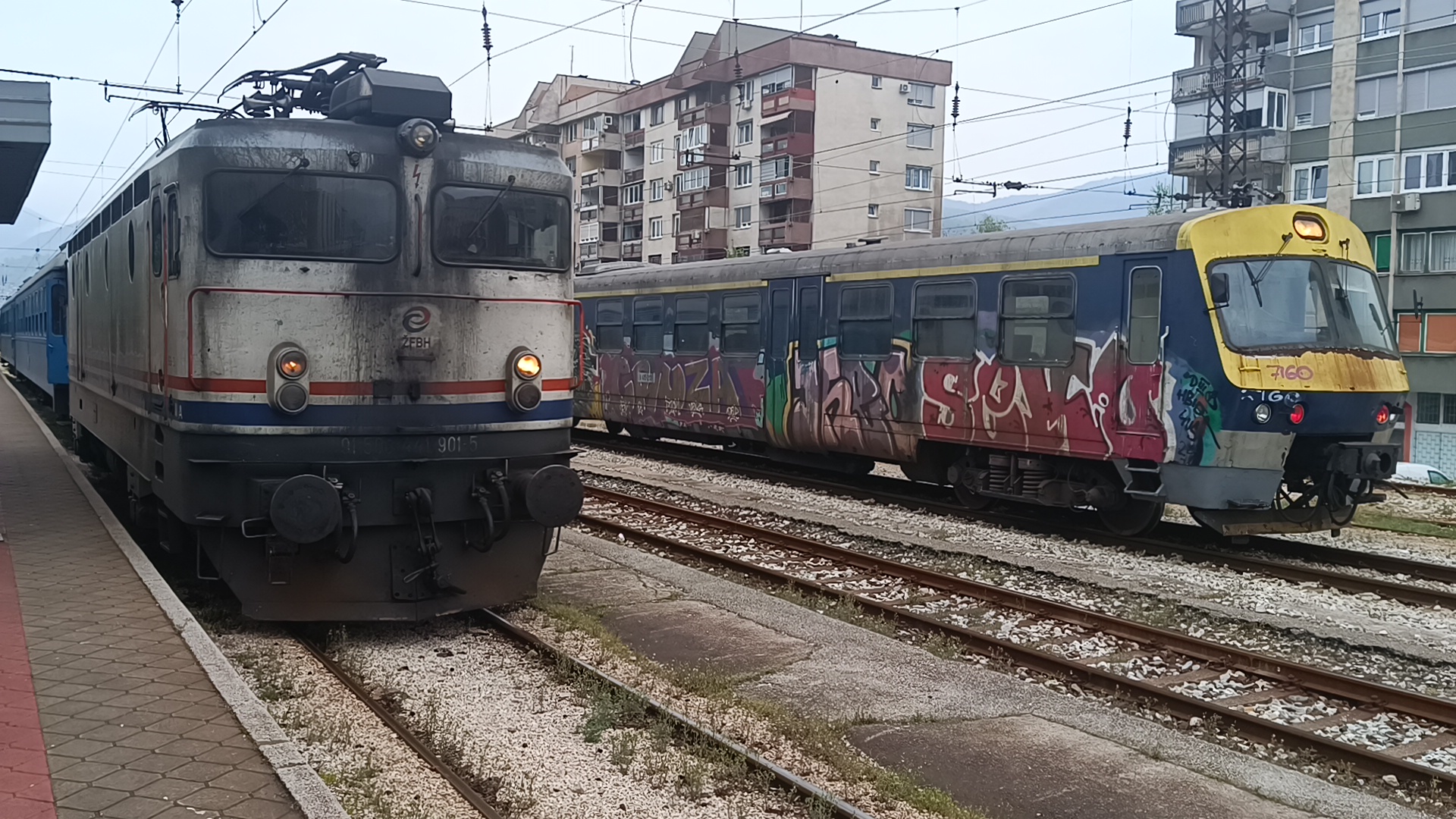 Zugverkehr im Bahnhof Zenica. Der lokbespannte Zug stammt aus den 60er Jahren und besteht aus zwei blauen Bahnwagen - ein Geschenk der Schwedischen Eisenbahn.